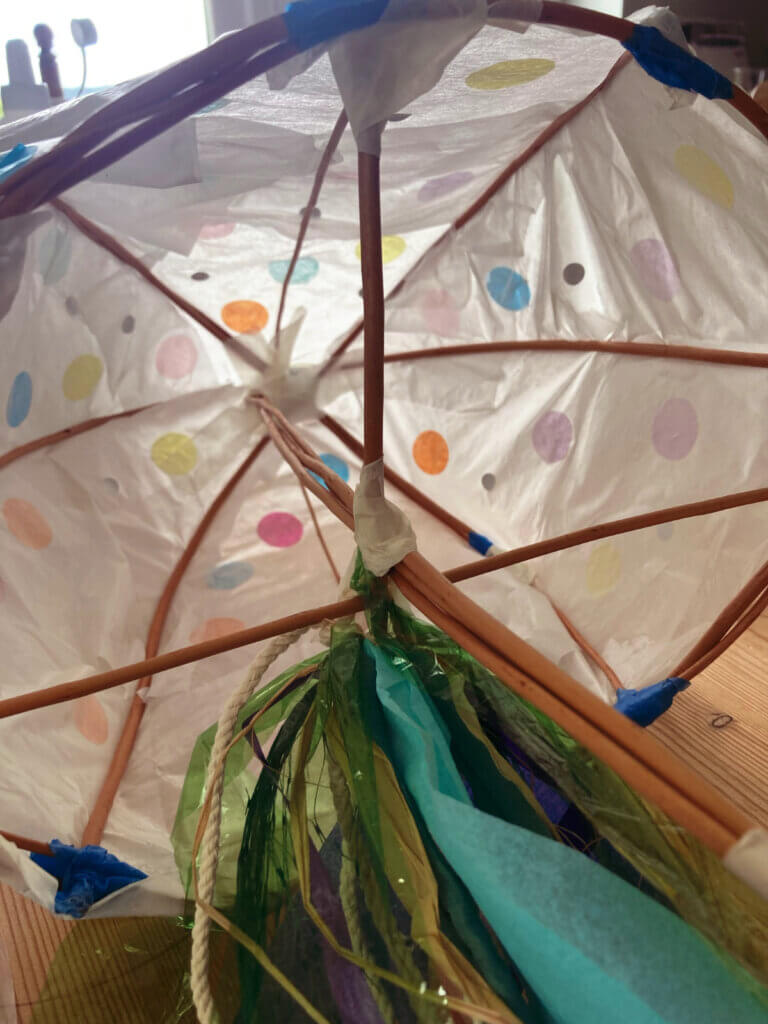 Close-up of the inside of a handmade lantern structure, showing a polka-dot paper covering, wooden framework, and colourful hanging streamers.