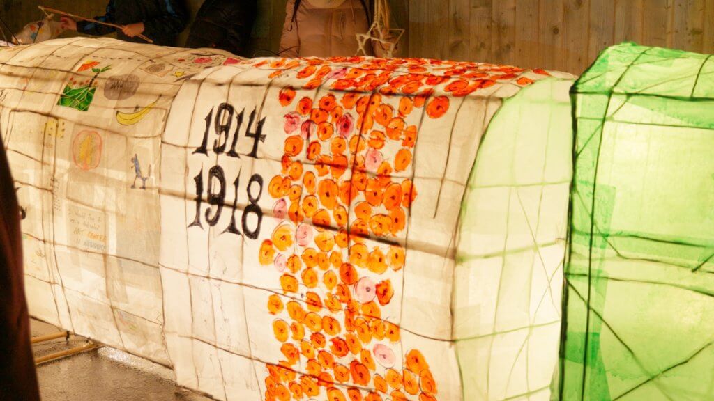 Close-up of an illuminated lantern shaped like a train carriage, decorated with painted poppies and the dates "1914–1918."